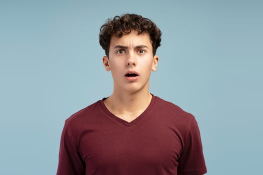 Worried, sad teen boy wearing casual red t shirt with open mouth posing isolated on blue background photo