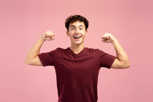 Portrait of happy attractive strong young boy with braces showing muscular arms with biceps, excited photo