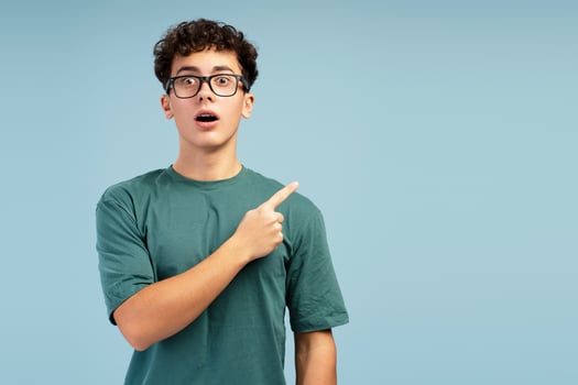 Portrait of excited, shocked teen boy wearing stylish eyeglasses, pointing finger on copy space photo