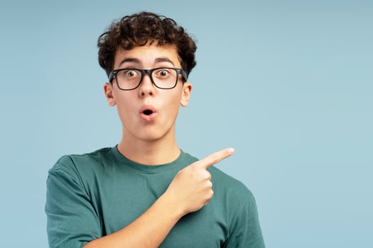 Portrait of shocked teen boy wearing stylish eyeglasses, pointing finger on copy space photo