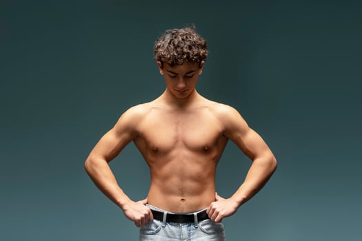 Attractive teen boy with naked torso, bare body, fashion model posing isolated on gray background photo