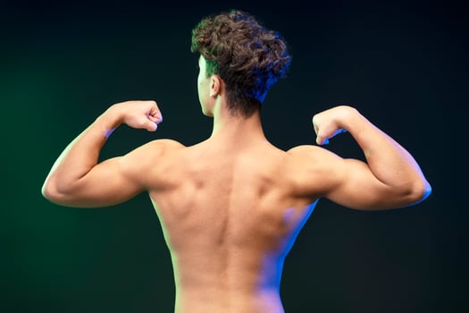 Back view, portrait of strong young boy, teenager showing muscular body isolated on black background photo