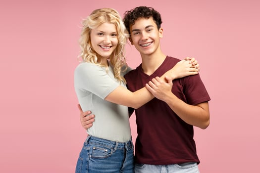 Beautiful couple, attractive young boy and girl hugging together, posing isolated on pink background photo