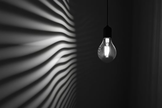 A Single Light Bulb Hanging Against a Wall with Curved Shadows photo