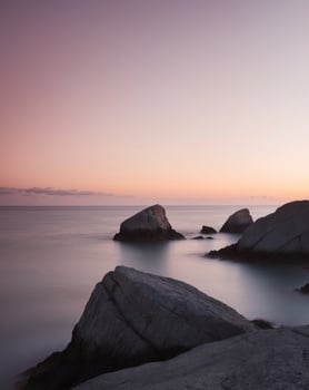 A long exposure photograph of rocks on the shore at sunset photo