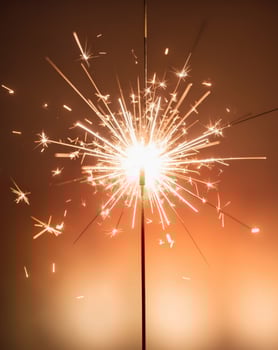 Burning sparkler emitting bright sparks with blurred orange lights in background photo