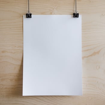 White paper hangs vertically on wooden surface, secured by black binder clips For Social Media Post Size photo