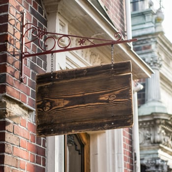 Wooden sign hangs on brick building, sunlight highlighting architectural details For Social Media Post Size photo