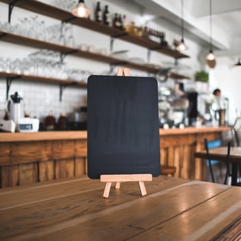 Wooden table holds empty chalkboard menu in cozy cafe, blurred background For Social Media Post Size photo