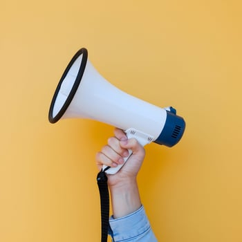 Hand holds white megaphone against bright yellow background, bold announcement suggested For Social Media Post Size photo
