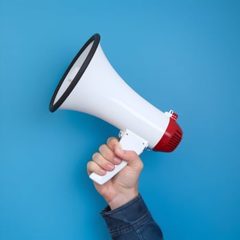 Hand holds white megaphone with red base, contrasting vibrant blue background For Social Media Post Size photo