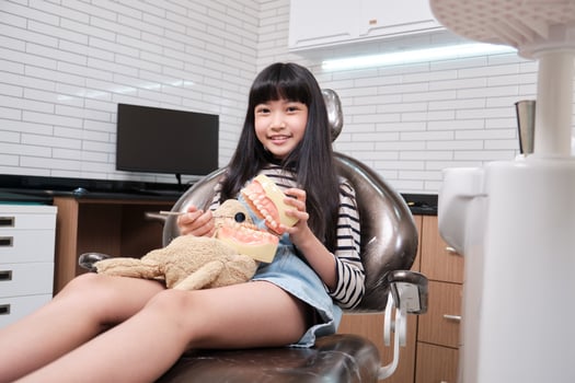 Cute Asian girl with doll play assumes dentist examines denture model, treatment and visits pediatric doctor in dental clinic, mouth and teeth hygiene, and orthodontic healthcare in kid hospital. photo