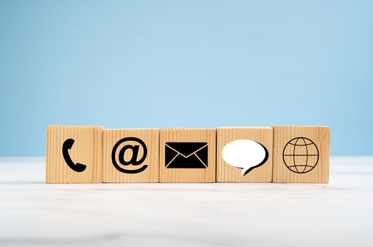 Close-up of wooden cubes with symbols of telephone, email, speech bubble, and the world on a marble floor against a blue background photo