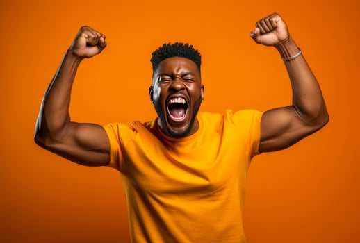 A dark skinned man with muscular arms raises his fists in triumph against an orange background photo