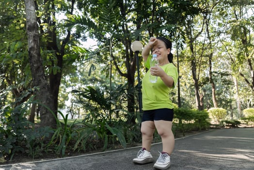 Petite Woman Jogging in a Lush Green Park on a Sunny Day, Staying Active and Healthy in Nature, Wearing Casual Sportswear and Holding a Water Bottle photo