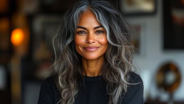 Confident woman with silver hair posing indoors. A woman with long silver hair smiles confidently while posing in a stylish indoor setting filled with decor. photo