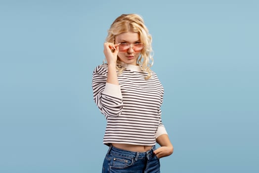 Happy blonde girl wearing casual sweater and stylish sunglasses posing isolated on blue background photo