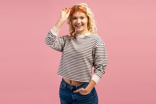 Positive teenager wearing stylish eyeglasses and casual sweater isolated on pink background photo