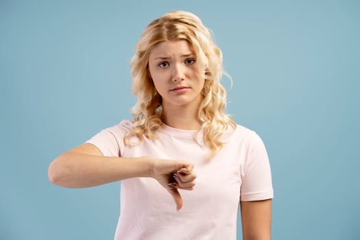 Unhappy, teenager, girl showing thumb down, looking at camera, posing isolated on blue background photo