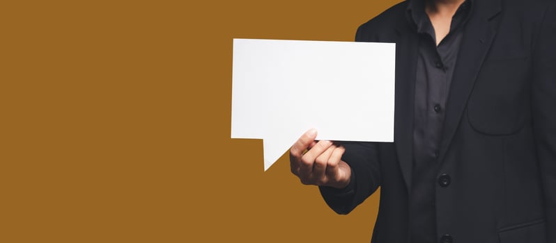 Businessman in a suit holding a blank white speech bubble while standing on an orange background photo
