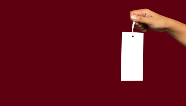 Hand holding a blank white label or price tag against a red background photo