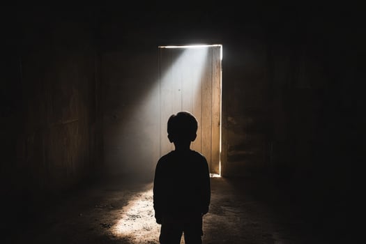 A boy standing in an empty room with light coming through the door photo