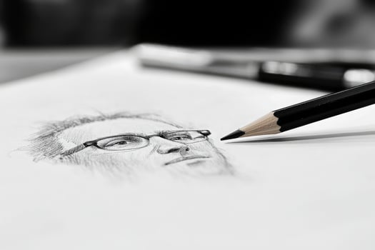 A detailed sketch of a mans face is being created with a graphite pencil on white paper. The focus is on the pencil tip near the drawing, highlighting a creative moment in a calm environment. photo