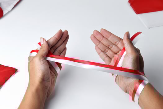 The hands of people praying are circled by a red and white ribbon photo