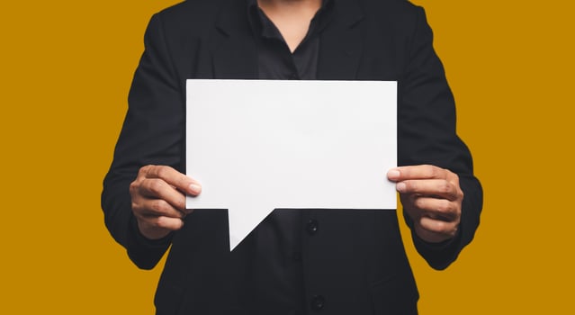 Businessman in a suit holding a blank white speech bubble while standing on an orange background photo