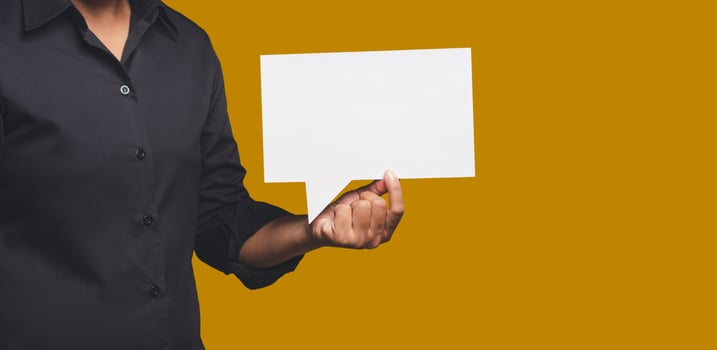 Close-up of hand businesswoman holding a blank white speech bubble while standing on an orange background photo