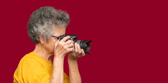 Senior woman taking photographs with a digital camera while standing on a red background photo