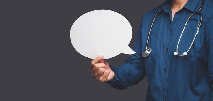 Speech bubble concept. Close-up of hand a doctor holding a blank white speech bubble against a gray background photo