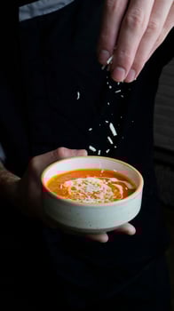 Chef adding garnish to a bowl of creamy orange soup in a cozy kitchen photo