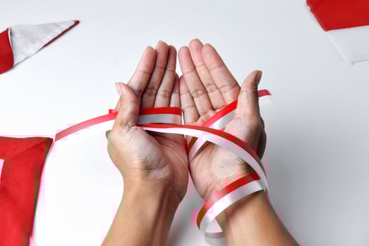 The hands of people praying are circled by a red and white ribbon photo