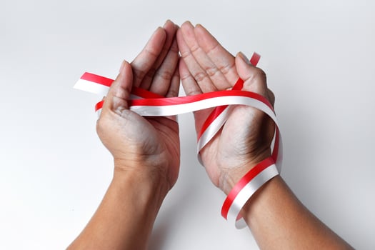 The hands of people praying are circled by a red and white ribbon photo