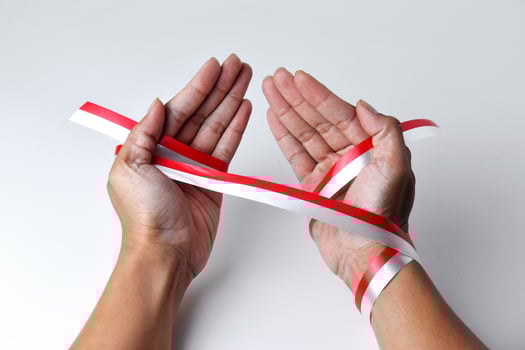 The hands of people praying are circled by a red and white ribbon photo
