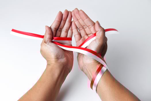 The hands of people praying are circled by a red and white ribbon photo