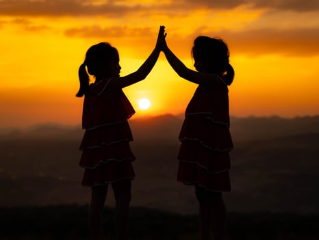 Silhouette of two little girls are happily playing on meadow during a summer sunset. Family love with colorful sunset. photo