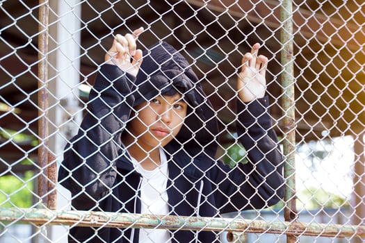 young Asian male wearing a brown hoodie had both hands on the iron mesh fence with a hopeless look in his eyes. Concept of quarantine, youth, control, isolation, freedom photo