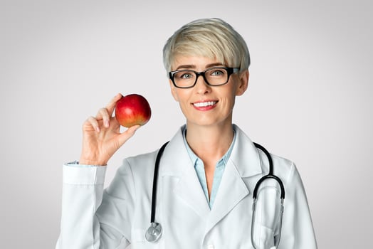 Healthy eating and diet concept. Adult woman doctor in glasses holds red apple in hand, panorama, free space photo
