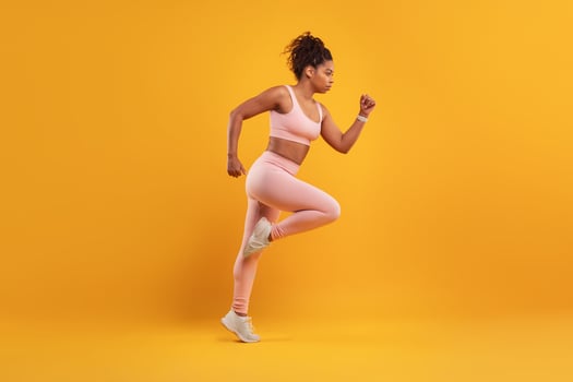 A woman in athletic wear is running energetically against a bright yellow background, showcasing her determination and focus during a workout. Her pose exudes strength and athleticism. photo