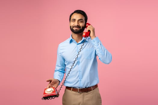 Attractive, happy Indian bearded man holding red phone, cellular, answering call looking at camera photo
