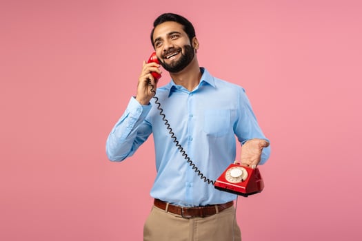 Portrait of smiling happy Indian bearded man holding red phone, cellular answering call looking away photo