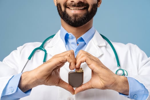 Smiling Indian man, doctor wearing white coat holding pacemaker, selective focus on hands photo