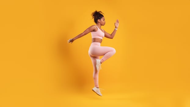 A woman in athletic attire exercises with enthusiasm against a bright yellow backdrop. She focuses on her fitness routine, showcasing strength and determination. photo