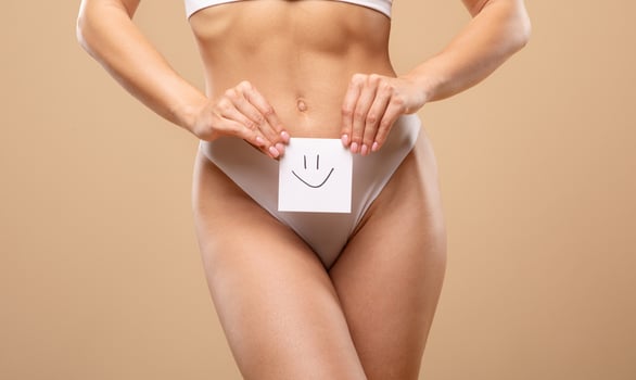 A young Caucasian woman poses gracefully in elegant lingerie, playfully holding a card with a smiley face. The neutral background enhances her beauty and confidence. photo