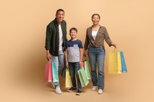 A loving African American family stands together in a studio, smiling widely. They are holding vibrant shopping bags, creating a warm and cheerful atmosphere of togetherness. photo