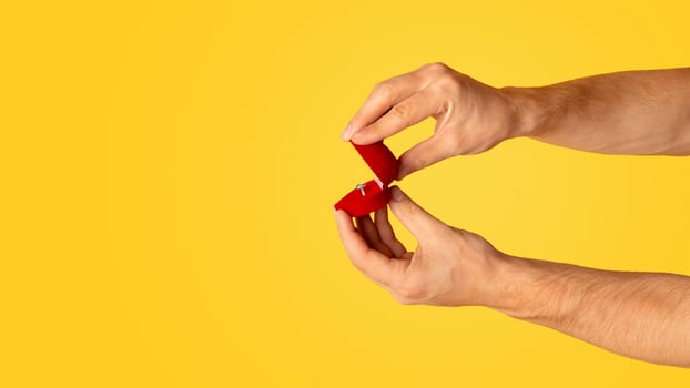 Closeup of millennial guy opening box with engagement ring on orange background, copy space. Panorama photo