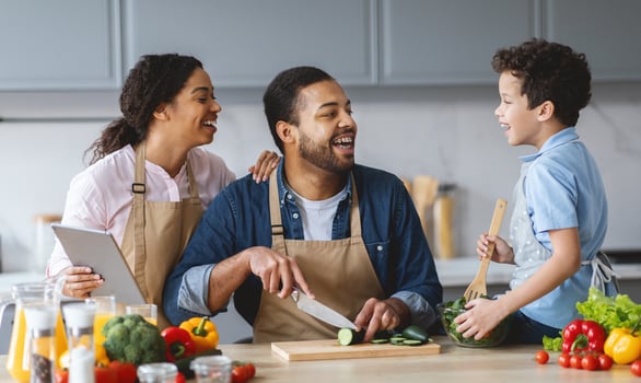 In a warm, inviting kitchen, a father happily prepares food while his wife and son share laughter and joy. This family is creating cherished memories during meal prep. photo