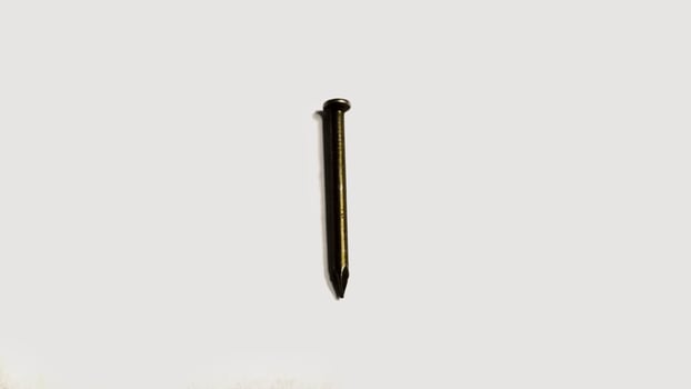 Close up of a single, dark colored nail isolated on a white background. Simple, minimalist image ideal for construction, DIY, or hardware concepts. photo